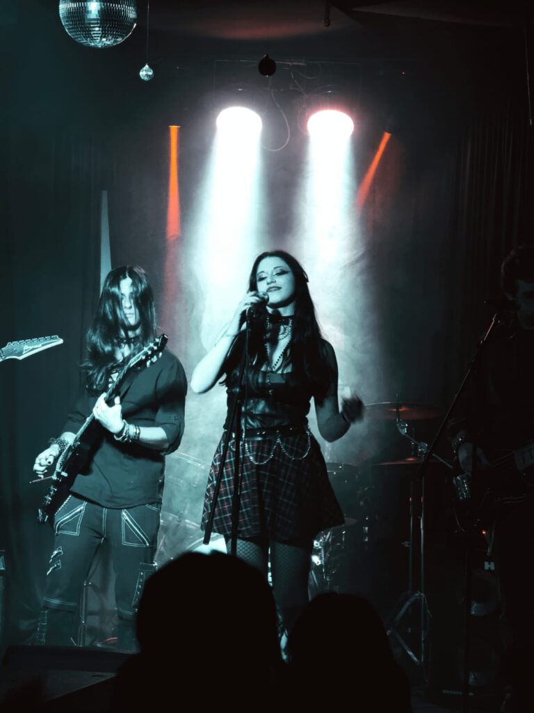 Cantante al microfono con chitarrista, luci bianche e arancio