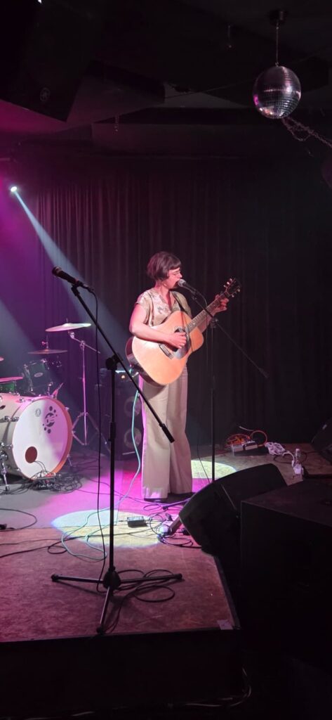 Cantautrice con chitarra acustica sul palco illuminato di rosa